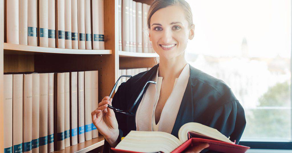 Leende kvinna, en advokat, som h책ller en bok i ett bibliotek